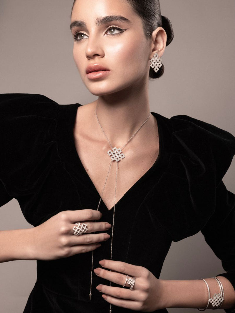 Woman wearing a necklace, ring, and earrings with a black outfit on a neutral background