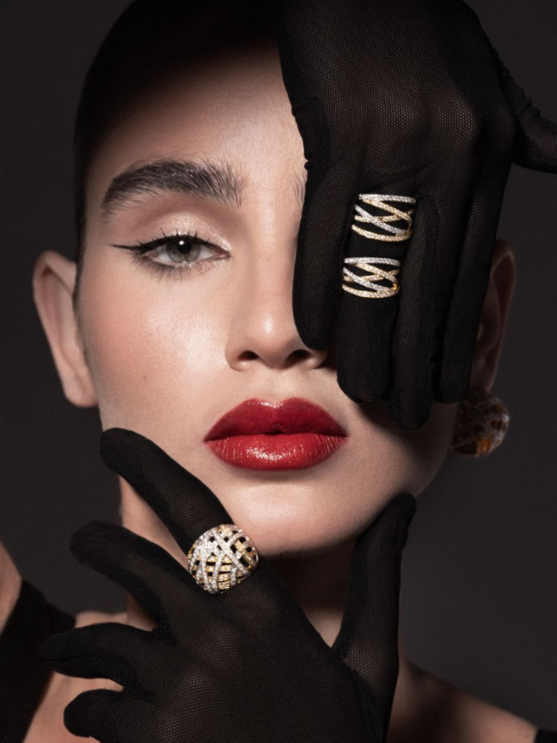 Woman with red lipstick and gold earrings, wearing black gloves with gold accents against a dark background